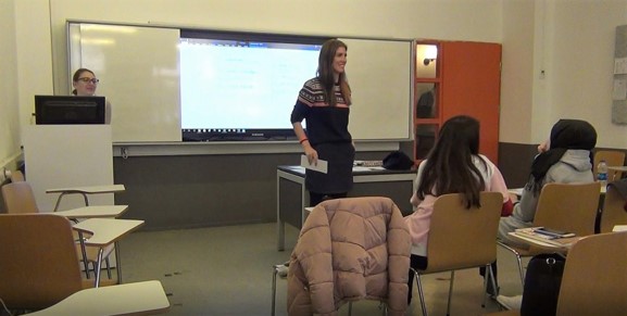 team teaching in esl classroom, one female teacher standing and smiling in front of the board, and the other one is in front of the computer